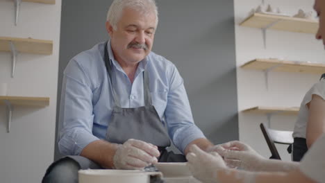 una mujer maestra comparte sus habilidades con un hombre mayor dirigiendo una lección para los ancianos. muestre al abuelo la técnica de trabajar en una rueda de alfarero con arcilla cerámica