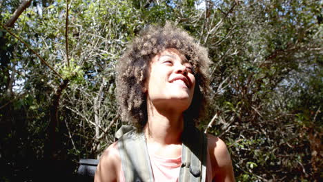 young biracial woman smiles brightly, surrounded by lush greenery