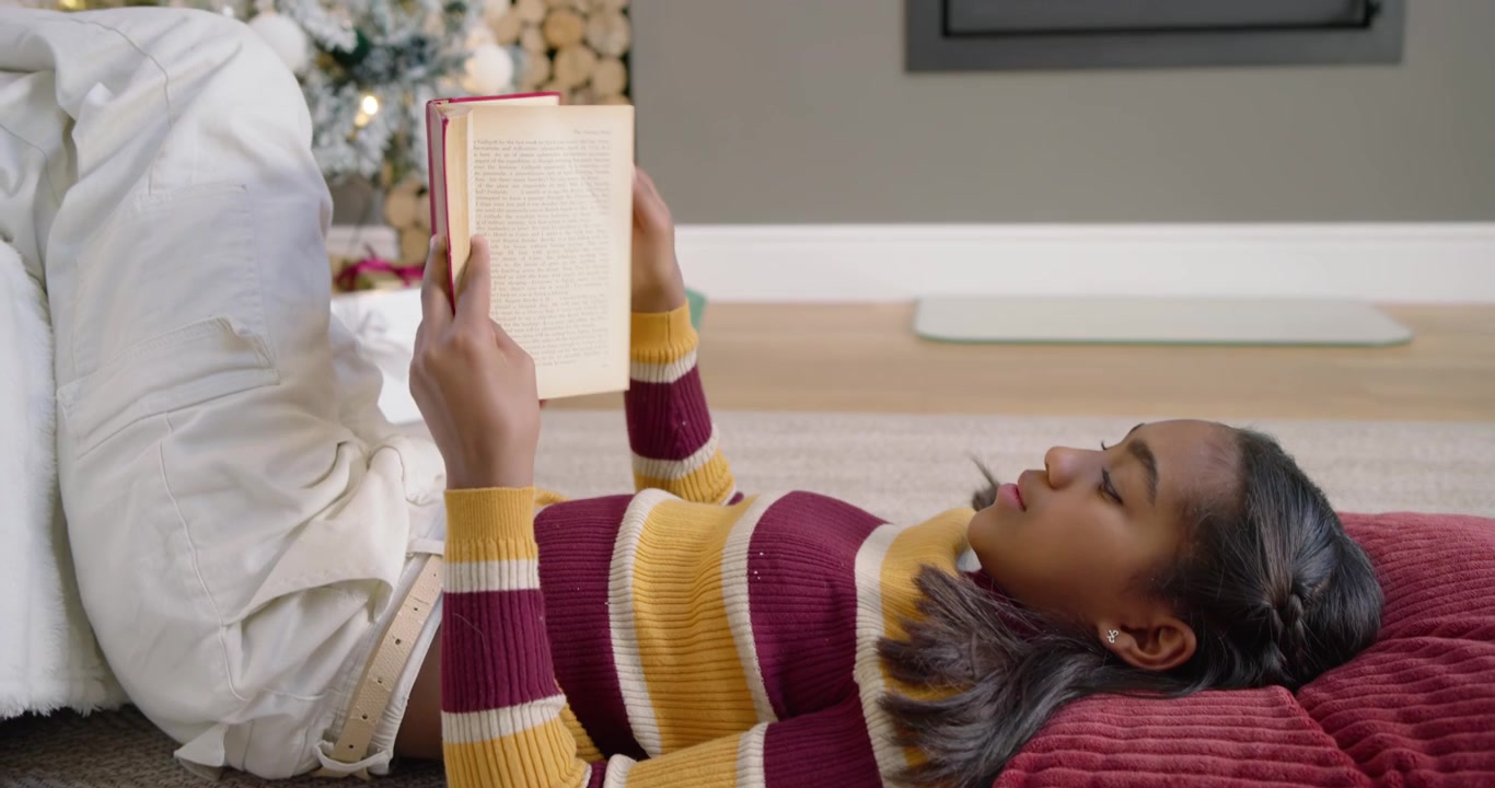 Adolescente Afro-Americana Abrindo a Página, Reagindo e Lendo um Livro no Tapete para Relaxar Perto da Lareira