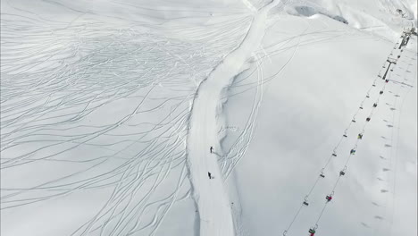 Luftaufnahme:-Zwei-Personen-Fahren-Mit-Dem-Skilift-Im-Alpenresort-Die-Pisten-Hinunter