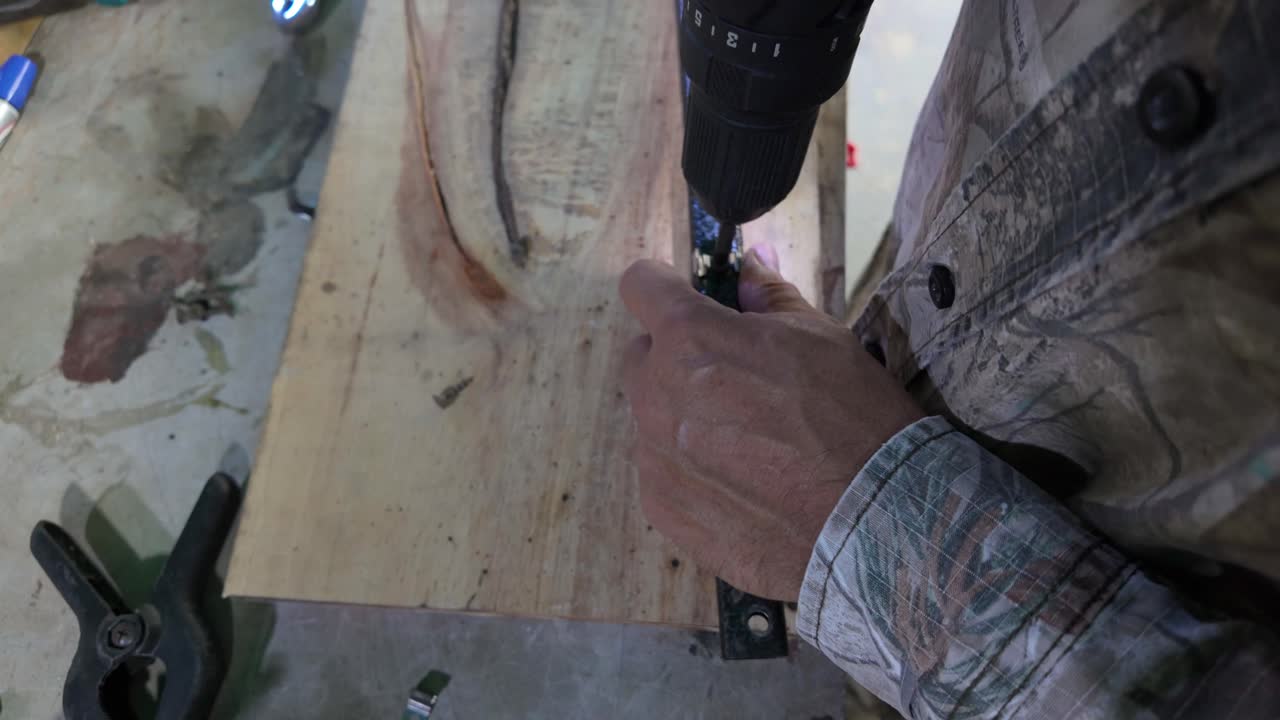 Worker uses a red power drill to bore a hole into a metal tube on wooden board