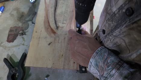 worker uses a red power drill to bore a hole into a metal tube on wooden board