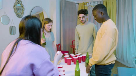 happy multiethnic young friends playing beer pong at home