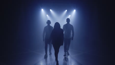 backlit silhouettes of singer vocalist girl, saxophonist sax, dj man with headphones walking forward