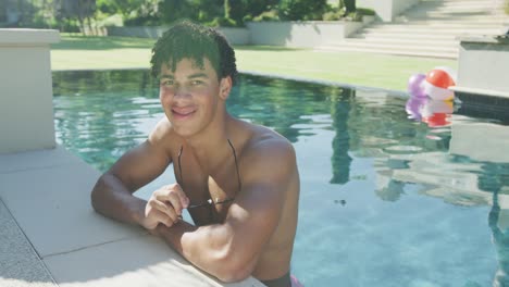 portrait of happy biracial man with sunglasses at pool in garden on sunny day