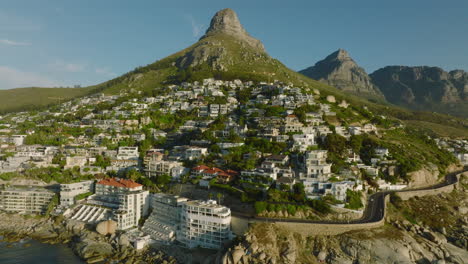 Diapositiva-Y-Toma-Panorámica-De-Lujosos-Apartamentos-En-Pendiente-Pronunciada-En-La-Costa-Del-Mar.-Montañas-De-Fondo.-Ciudad-Del-Cabo,-Sudáfrica