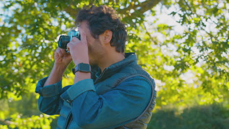 mature man in autumn countryside taking photo on retro style digital camera to post to social media