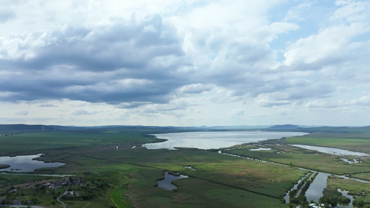 Expansive wetland landscape dotted with interconnected lakes, winding channels, and green fields under a dramatic sky