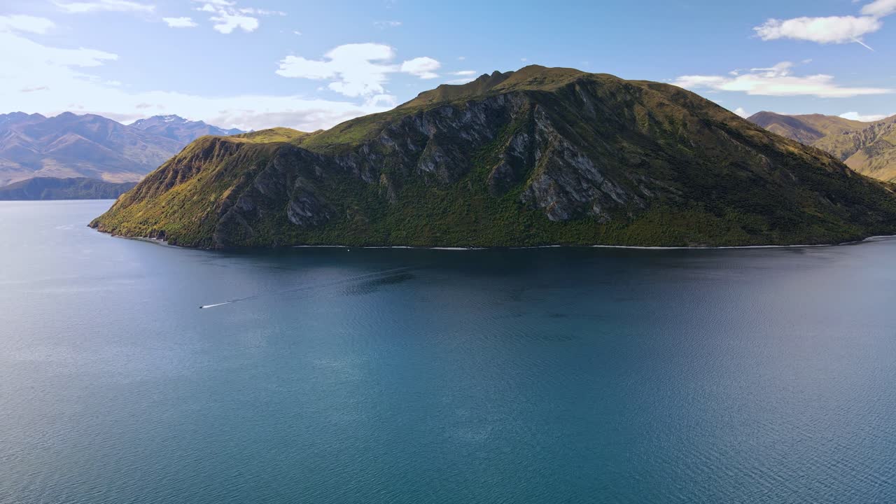 High drone pullback revealing Lake Wanaka island with blue water and mountains