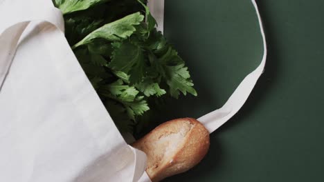 Video-of-white-canvas-bag-with-parsley,-kale-and-baguette,-copy-space-on-green-background