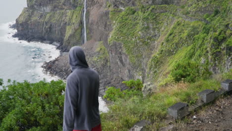 hooded man walks out to overlook revealing véu da noiva waterfall, slow motion