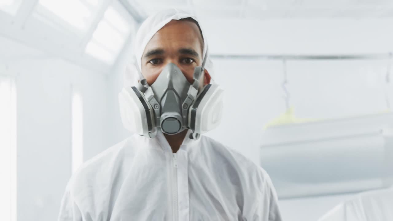 mecánico de coches de raza mixta poniendo ropa de protección y mirando a la cámara