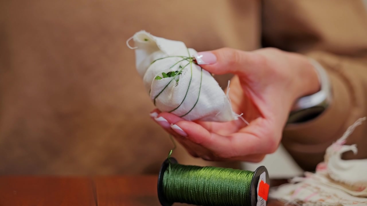 Young woman binds blooms to Easter egg before wrapping it gently in soft gauze