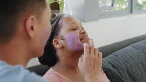 young asian man applies a facial mask to a young biracial woman at home