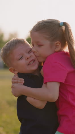 adorable little children hug on green meadow at sunset light slow motion. brother and sister love. happy friends spend time in park