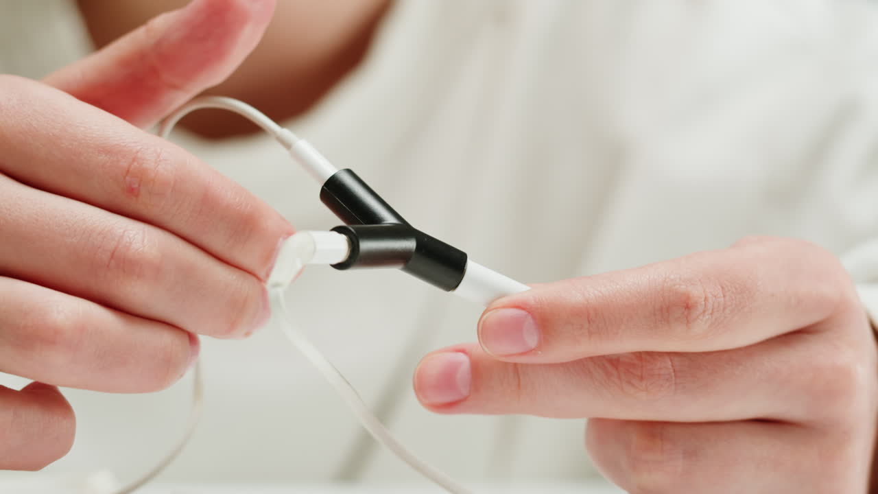Young woman trying to untangle the headphones close-up. Special adapter for headphone. Tangled wires on table. Trying to untangle many messy cables
