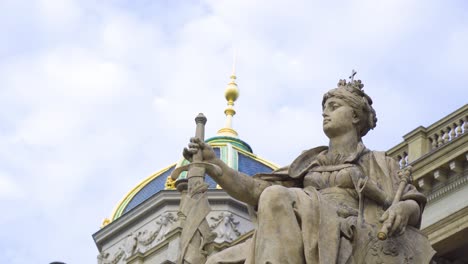 woman statue sitting down on a throne holding a sword in front of her wearing a crown with a cross at the background a building with golden tower pointed top and details made by professional