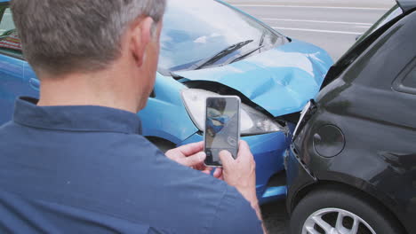 motorista masculino involucrado en un accidente automovilístico tomando fotos de los daños para una reclamación de seguro