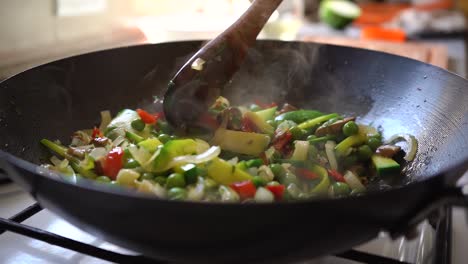 cooking and mixing healthy vegetables with green peas in a pan using wooden spoon. close up