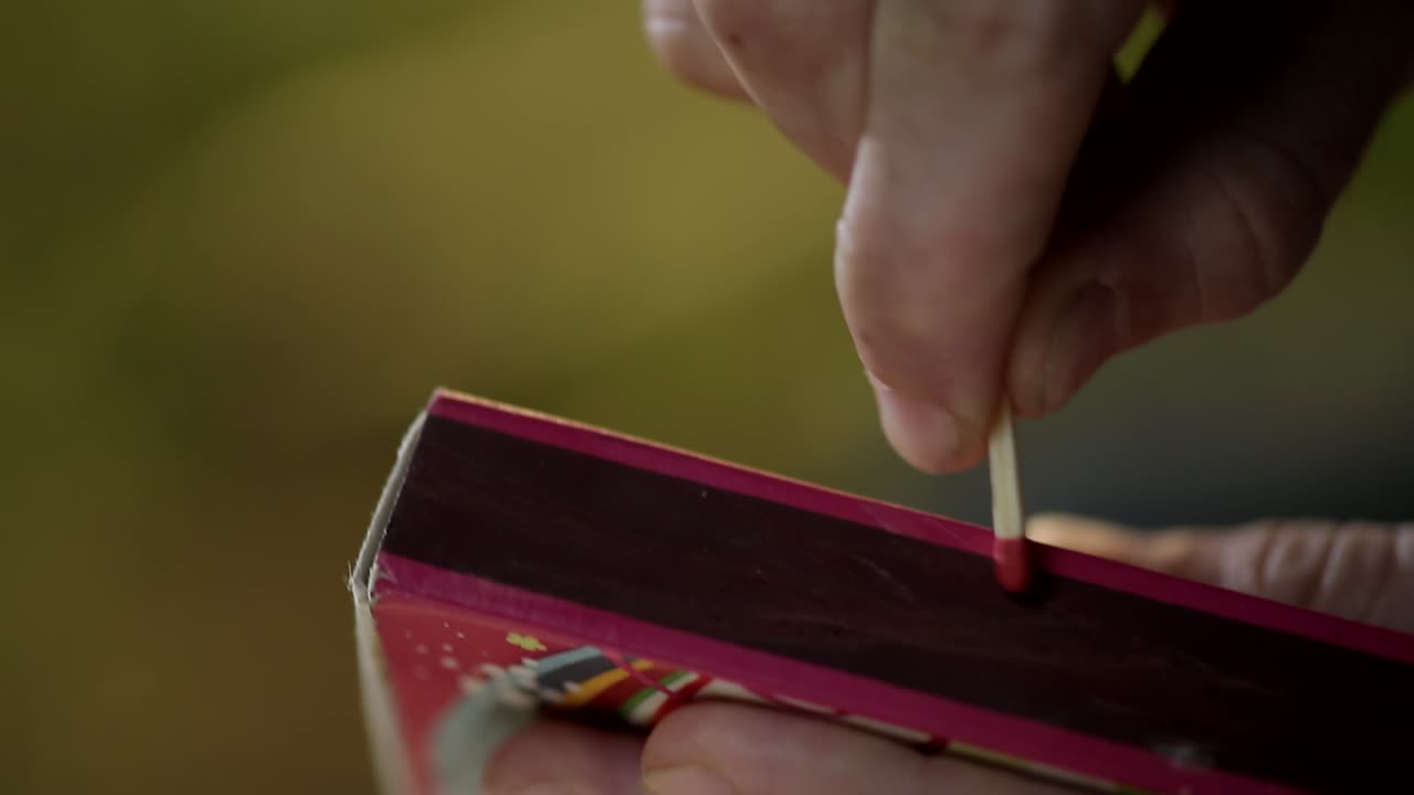 primer plano de una mano no identificada golpeando una cerilla sobre una caja de cerillas para encenderla