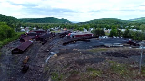 an aerial view of an abandoned narrow gauge coal rail road with rusting hoppers and freight cars and support building starting to be restored