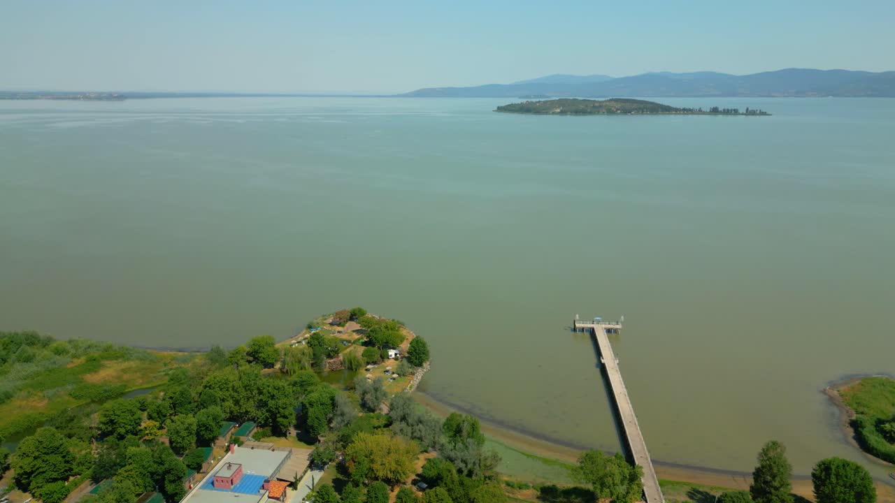 Serene aerial perspective revealing isola maggiore island nestled within lake trasimeno's tranquil waters, showcasing pristine landscape and scenic pier against mediterranean backdrop