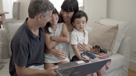 padres alegres y dos niños sentados con una computadora portátil en el sofá