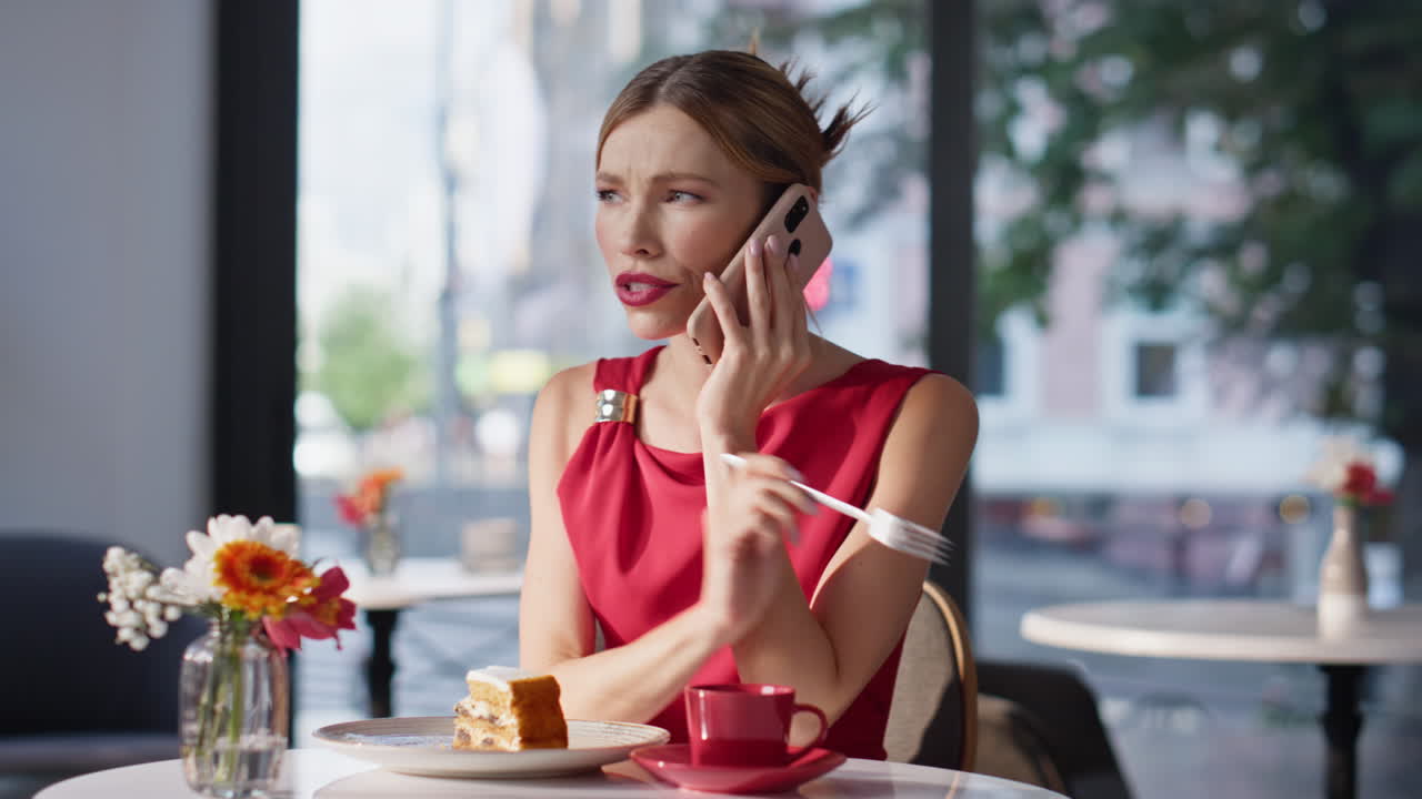 Calling woman eating cake wearing red dress in luxury restaurant closeup