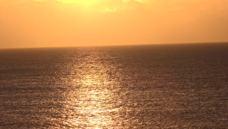 Sunset-reflecting-on-ocean-surface-in-mellow-orange-colour-with-bright-orange-sky-in-the-background