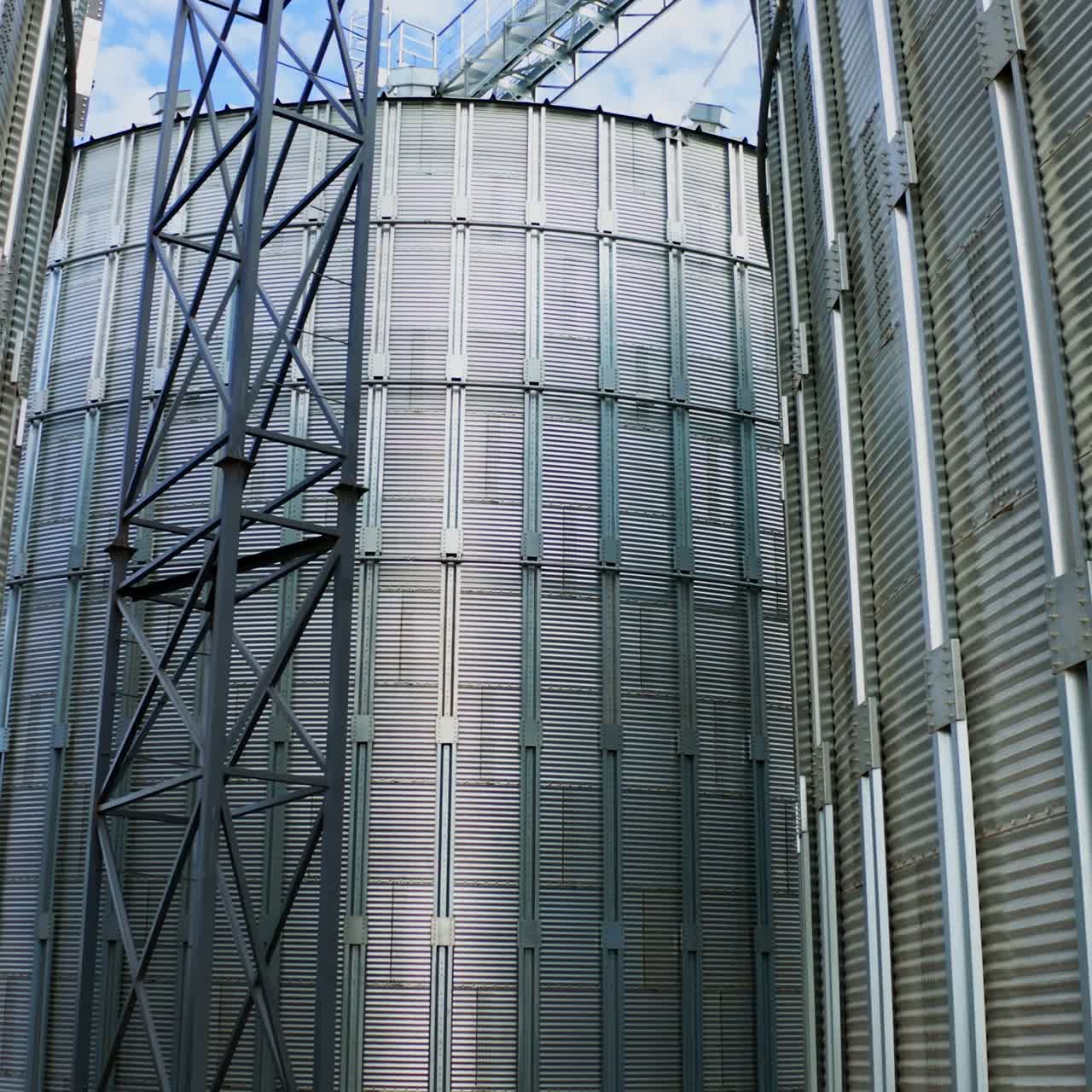 Exterior of modern plant. Large metal grain elevators outdoors. Aluminum containers for storing and processing crop. Close-up.Camera rising up.