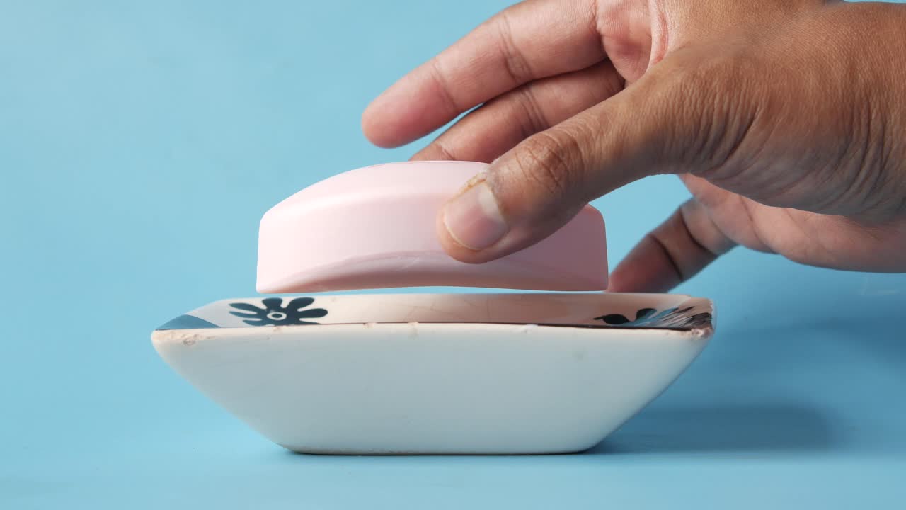 색 비누 접시 에 분홍색 비누 를 들고 있는 손