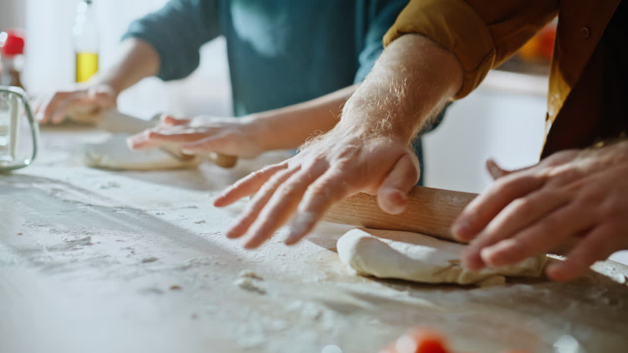 Family hands making dough kneading using rolling pin at home countertop closeup
