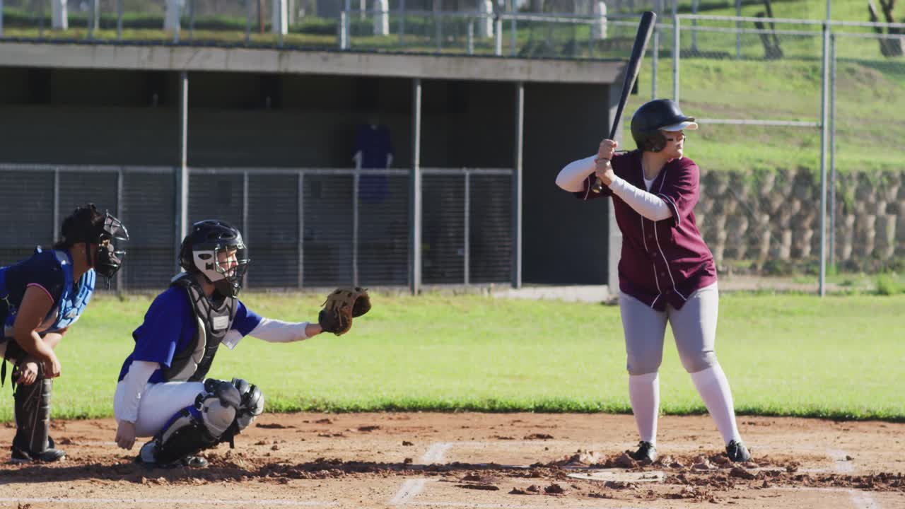Gruppo eterogeneo di giocatrici di baseball che giocano sul campo, battitrice che colpisce la palla lanciata.