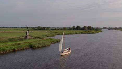 Sailing-boat-on-canal-at-Alde-feanen-friesland-passing-by-a-windmill,-aerial