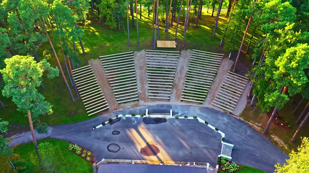 Open-air amphitheater with wooden seating with surronded trees, aerial top view