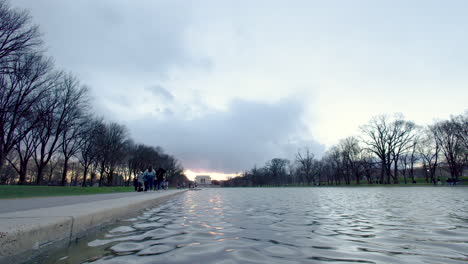 people are walking along the edge of the reflecting pool in washington dc with lincoln memorial in distance - ultra-wide shot