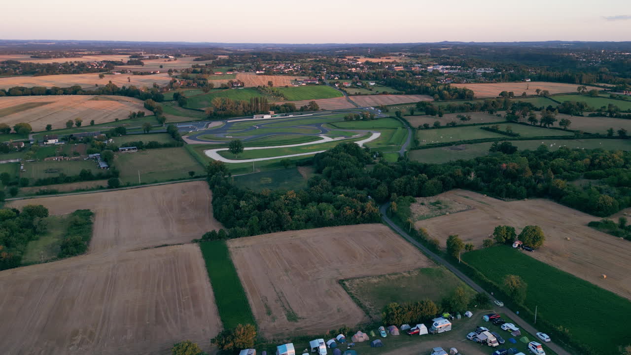 Linear Tilt Aerial View of Camping Lot in Rural Area with Green Field and Racing Track in Background at Music Festival