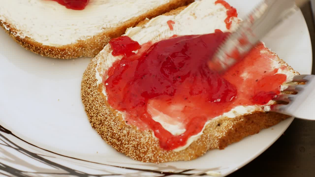 Studio: delicious strawberry jam being spread by silver knife on bread and butter