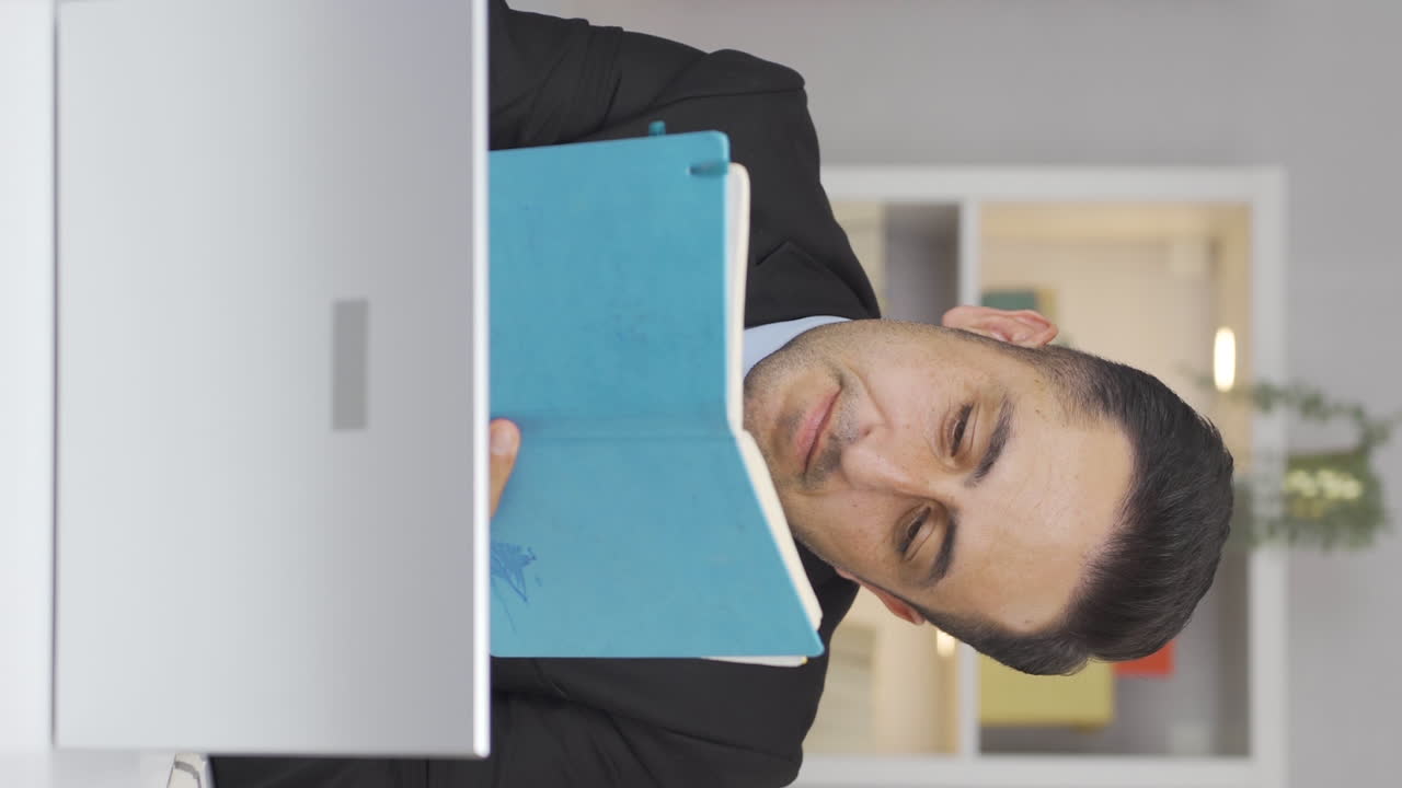 홈 오피스 직원 남자가 메모를 하고 정보를 기록하는 수직 비디오입니다.