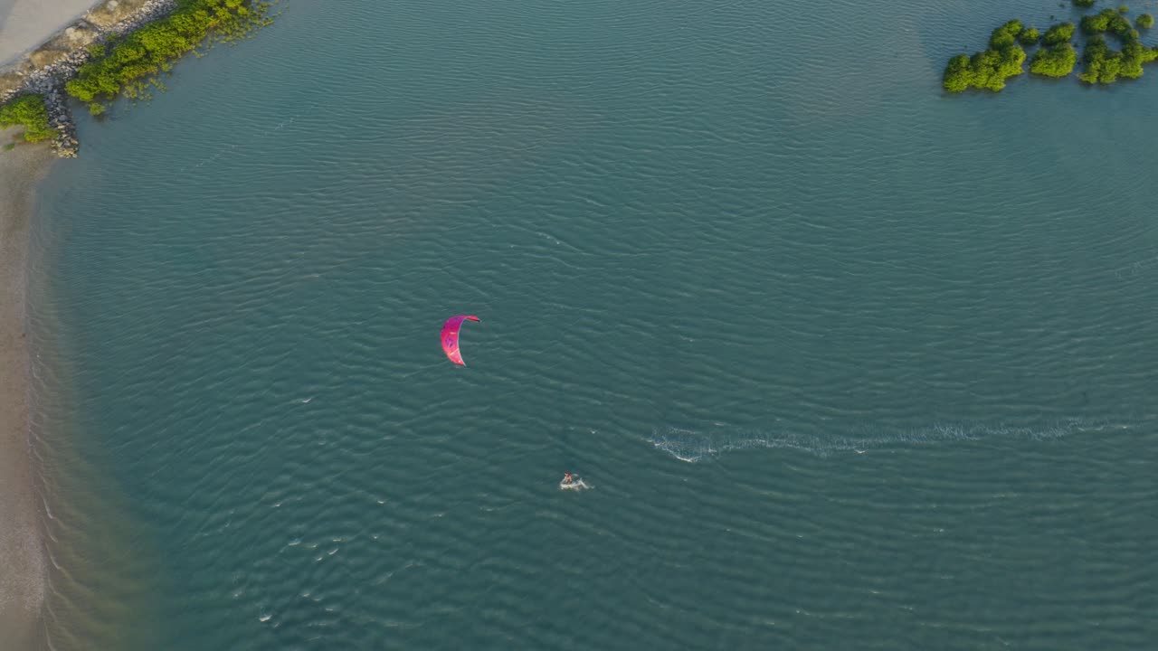 Kitesurfer riding across flat lagoon water near Ilha do Guajiru in Itarema municipality Ceara state Brazil South America leaving wake trail on smooth surface drone top down drone tracking