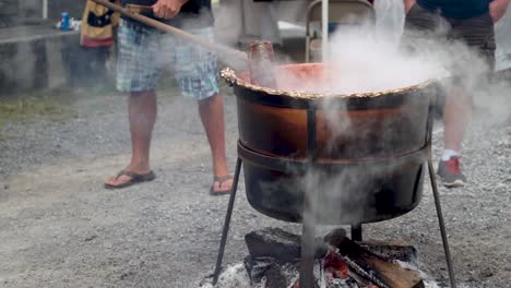 closeup of someone stirring steaming apple butter in a large wood fired cauldron outside