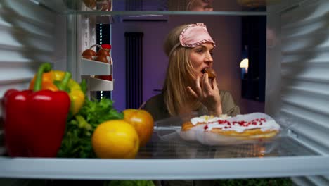 mujer comiendo una rosquilla por la noche delante del refrigerador