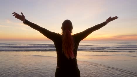 woman spreads her arms and breathes watching the sunrise