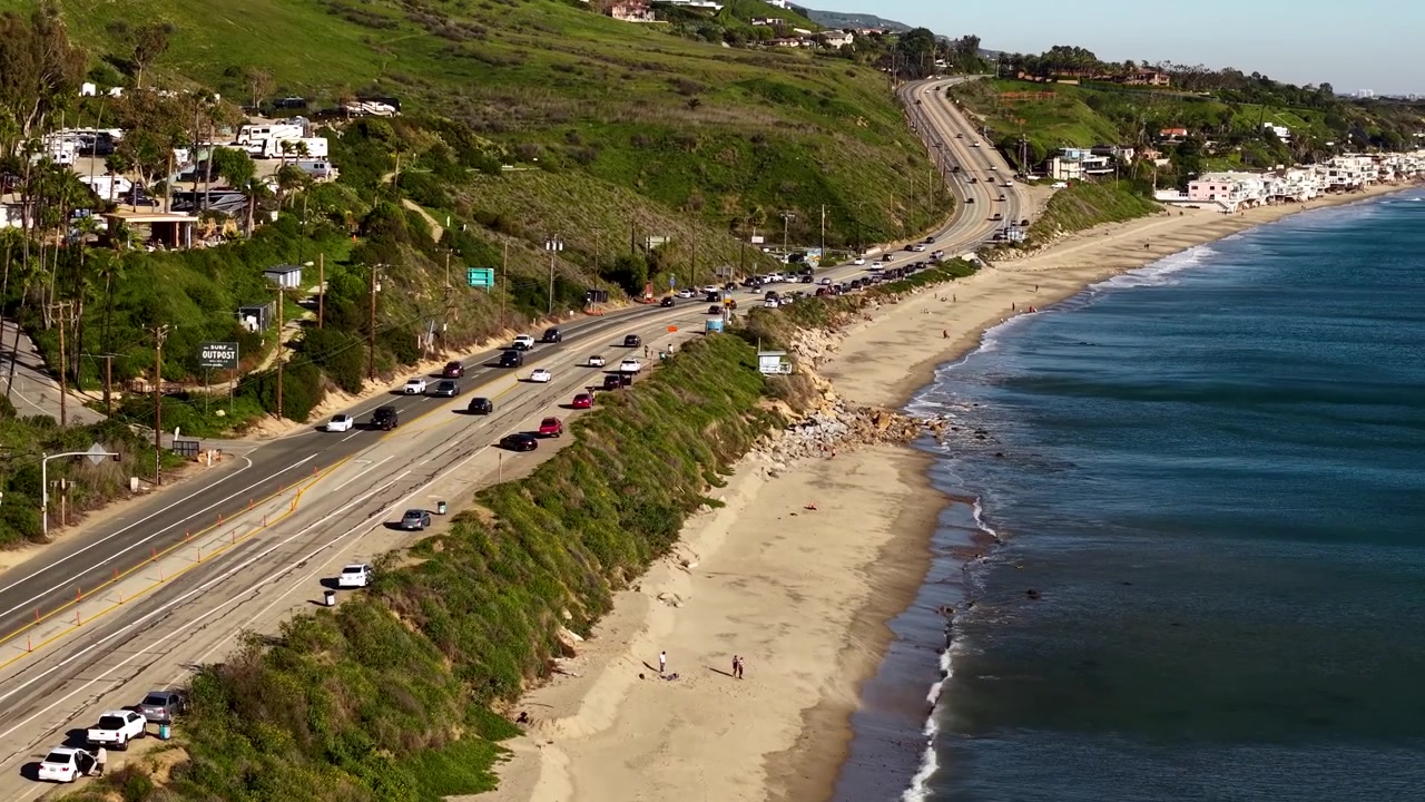 Traffico sulla Pacific Coast Highway lungo la costa di Malibu, il drone si muove parallelamente alle auto sulla rotta costiera più panoramica della California