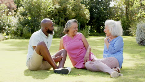 sitting on grass, three senior friends enjoying conversation in park