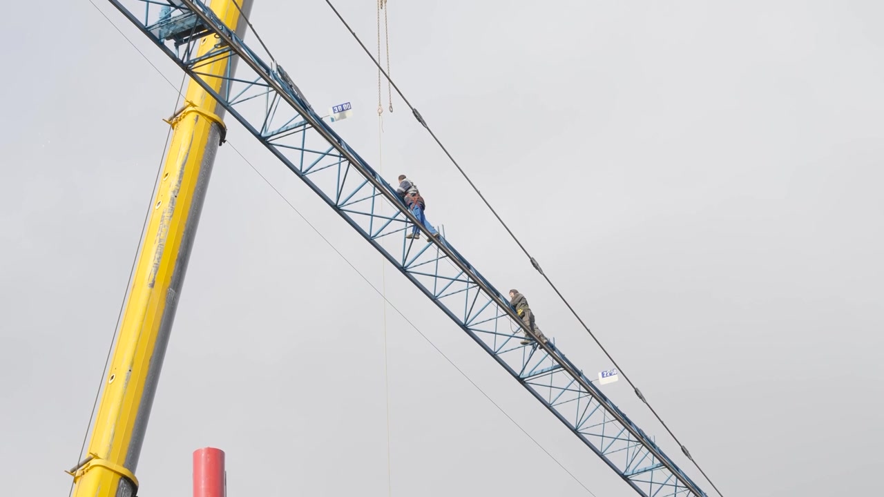Close-up video footage of construction workers performing tasks on a crane at an active building site.