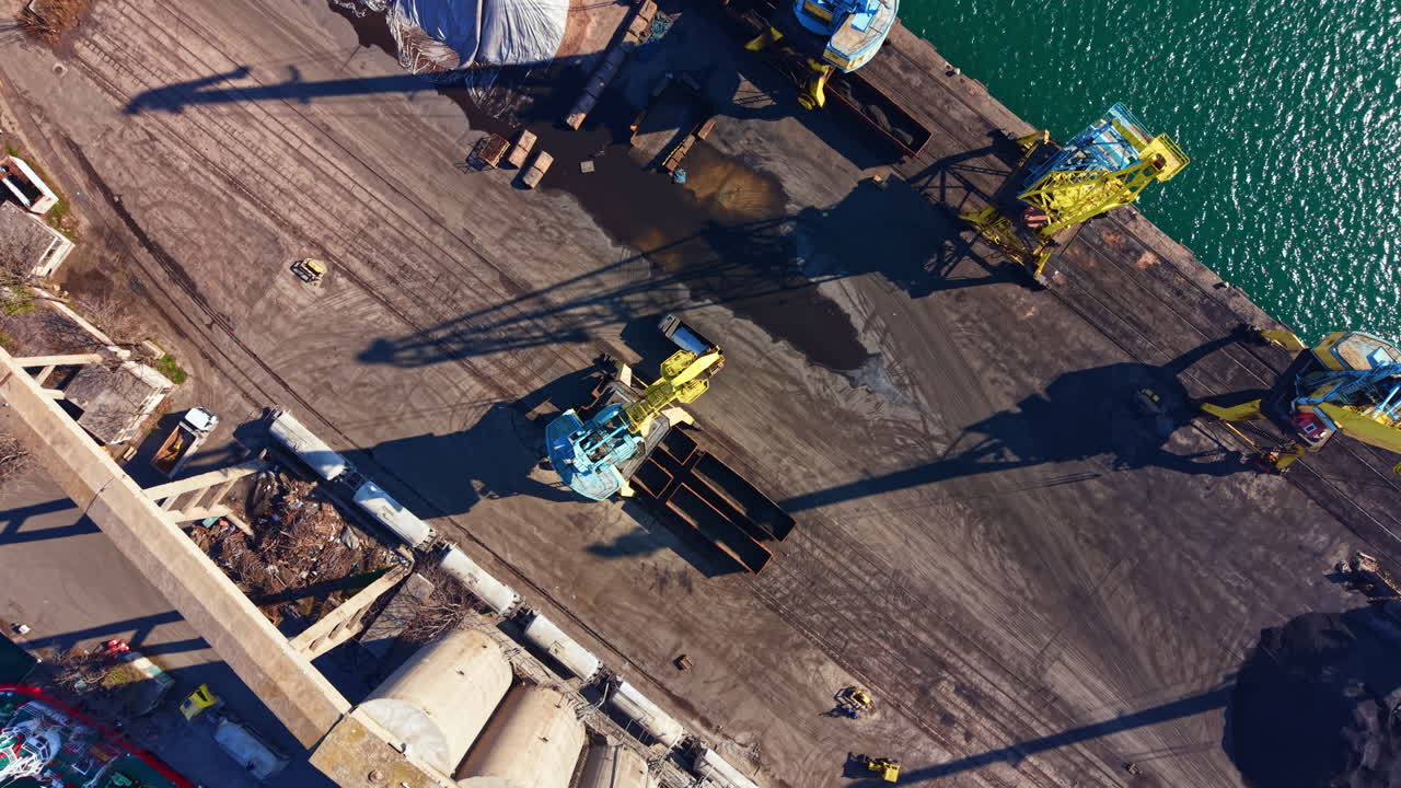 Gru e macchinari lavorano in un porto trafficato durante le ore diurne.