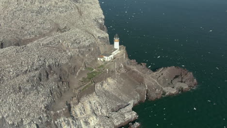 An-aerial-view-circling-Bass-Rock-and-lighthouse-as-gannet-seabirds-circle-their-island-colony-on-a-sunny-day,-East-Lothian,-Scotland