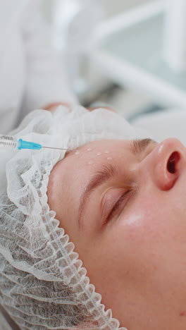 cosmetólogo aplicando suero de una jeringa en la frente preparándose para el procedimiento de dermapen con microagujas