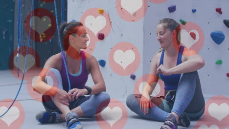 múltiples iconos de corazón flotando contra dos mujeres caucásicas en forma golpeando el puño en el gimnasio